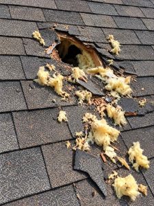 A damaged roof with with torn shingles and insulation debris around the opening.